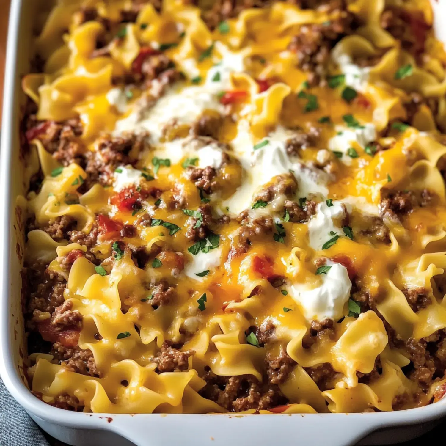 Close-up view of a baked casserole dish with layered noodles, ground beef, and melted cheese topped with parsley.