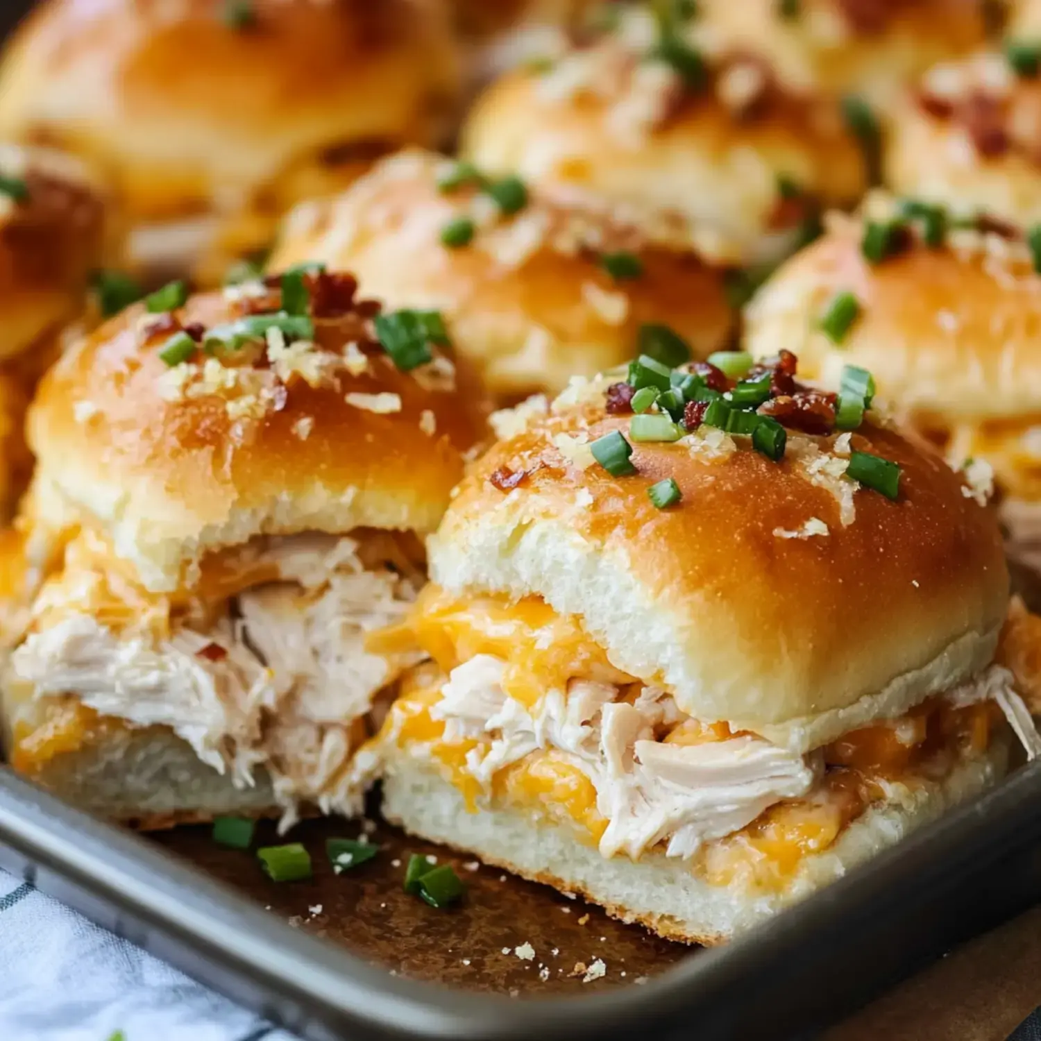 Close-up of chicken sliders on soft buns with melted cheese, crispy bacon, and green onion garnish, placed on a serving tray.